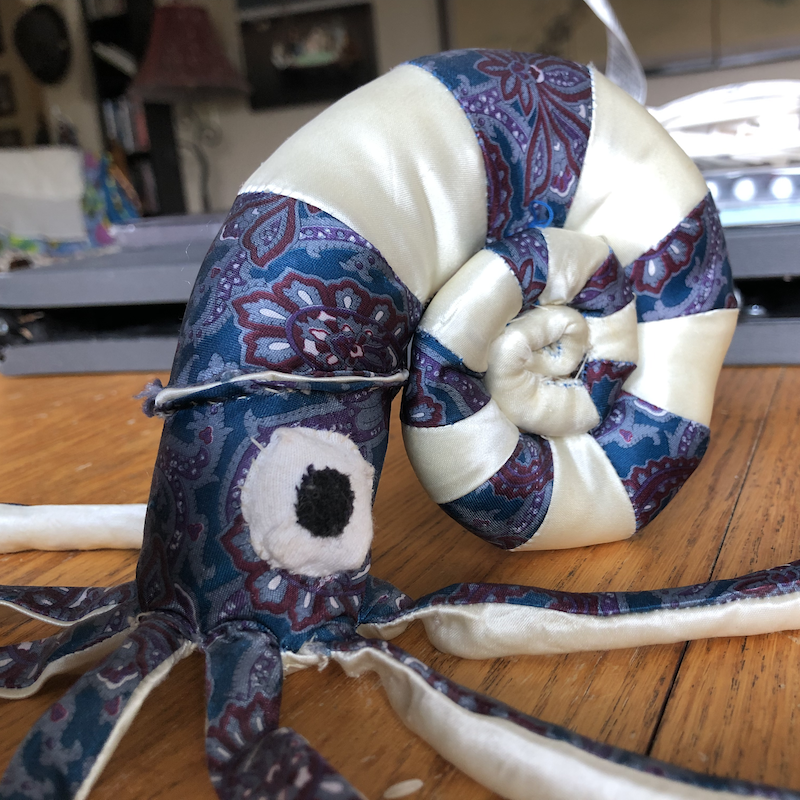 A plush of a blue squid creature inside a nautilus shell. Picture links to project page.