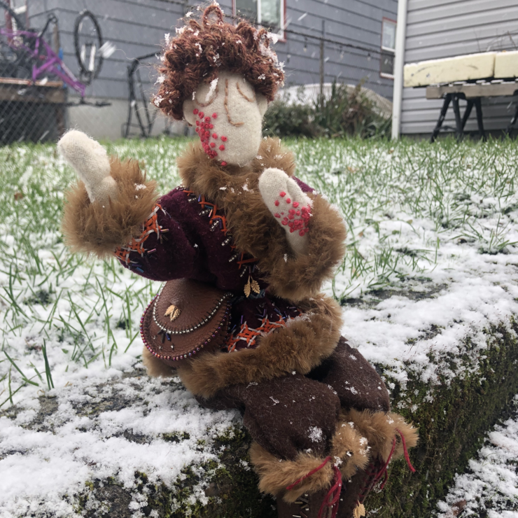 A small cloth doll in red and brown viking attire, trimmed with furs and elaborate embroidery, sits in the snow. Link takes you to project page.