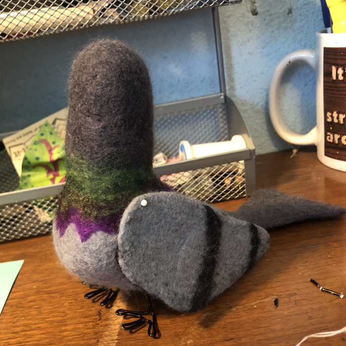A wool felted pigeon, with wire legs and no face, sits on a desk. Link takes you to project page.