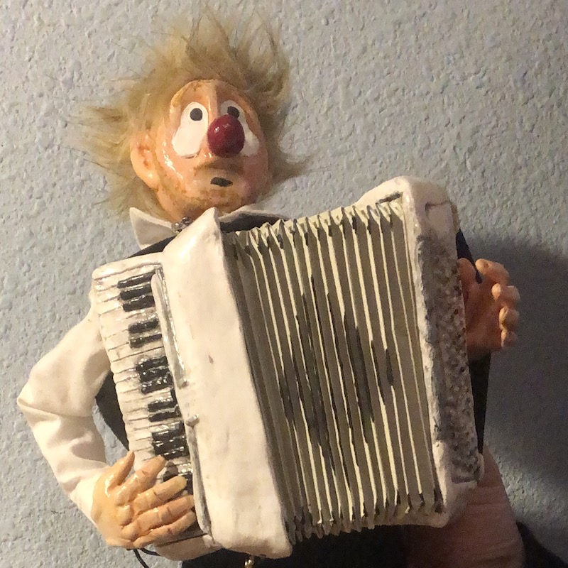 A small humanoid puppet from the waist-up. A clown with messy blond hair, a big red nose, and a white collared shirt. He plays a large white accordion. Picture links to project page.