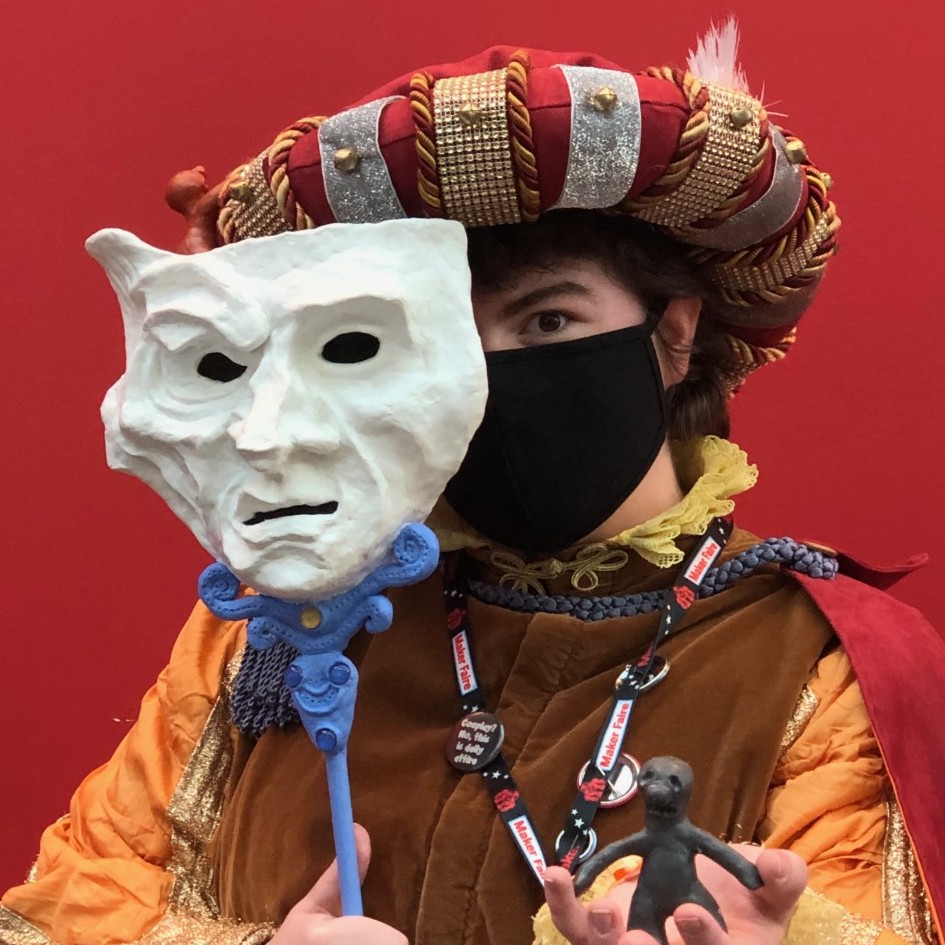 A person dressed in Medieval costume, holding an unsettling white clay mask halfway in front of their face with one hand, and a small clay figure in the other. Link takes you to project page.