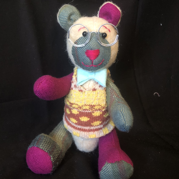 A small teddy bear made of magenta, green, and tan fabrics, wearing a sweater vest and little wire spectacles. Picture links to project page.